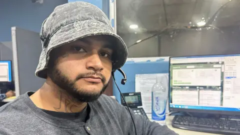 BBC Alberto Salagan, who is wearing a hat, looks at the camera while sat at his desk