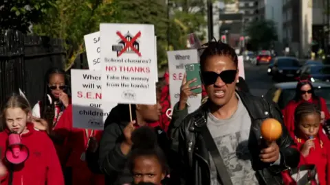 BBC A woman and a group of children holding up signs urging the council to keep the school open