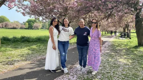Julia Bryson/BBC Four women stand on a path on a park in Harrogate, underneath cherry blossom trees.