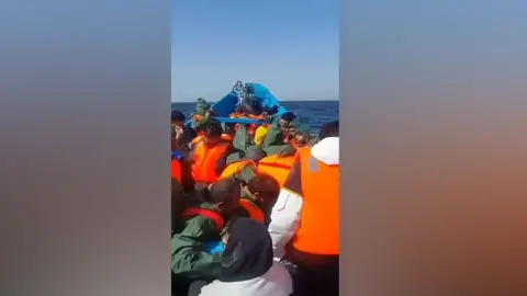 A screengrab from the boat shortly after it left Mauritania. There are many migrants wearing orange lifejackets, all facing away from the camera.