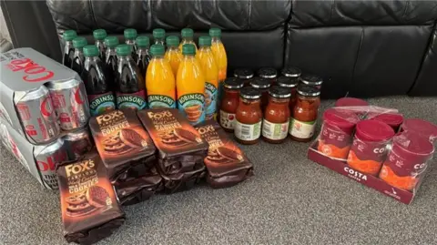 Sally Marie in Greater Manchester Two eight packs of Diet Coke are shown on a grey carpet, next to six packets of Fox's half coated chocolate cookies, ten jars of Loyd Grossman tomato and basil pasta sauce, 15 bottles of Robinsons squash and six tubs of Costa coffee.
