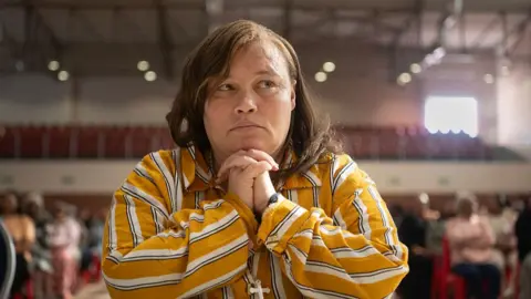 AFP Kelly Smith sit in a courtroom with her hands clasped, wearing a striped shirt.
