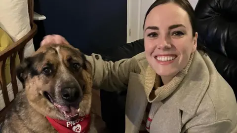 Facebook Marissa Keltie pats the head of a dog, while both look into the camera. Marissa is grinning.