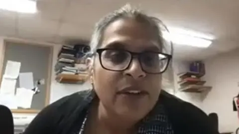 Orthopaedic Academy A video shot of Kuldeep Stohr giving a lecture to Orthopaedic Academy. She wears brown glasses and has hair tied back in a ponytail, wearing a black cardigan.