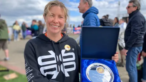 Chris Radburn/BBC Vicki Riley smiles as she holds up her medal. She wears a sweatshirt and around her are onlookers.