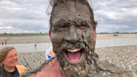 Chris Radburn/BBC Joel Hicks has a face full of mud. it's stuck in his beard and hair and on his teeth.