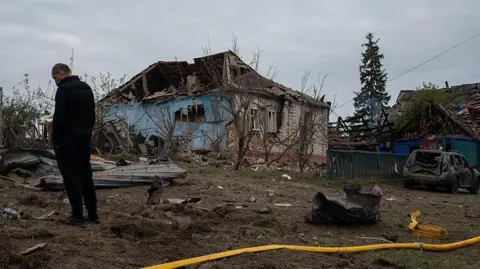 Getty Images A man stands amid debris in front of residential houses destroyed by Russian shelling on May 6, 2025 in Velyka Chernechchyna, Sumy Oblast