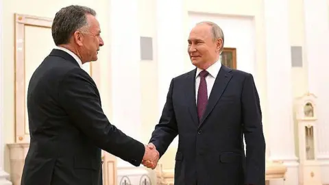Getty Images Two men in dark suits, Putin on the right, shake hands in the Kremlin in Moscow in April