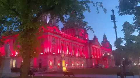 Belfast City Hall picture at dusk, lit up in red to commemorate VE Day.