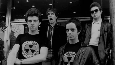 Getty Images Four young men, two of whom are wearing The Vapors t-shirts. One man is yawning. The image is in black and white.
