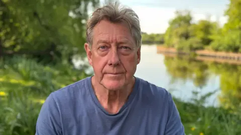 Fishing club member Gary Cyster, in a blue t-shirt, sits on the bank of the River Trent.
