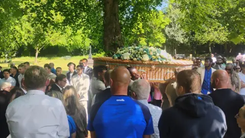 Pallbearers carry Joe Thompson's coffin as crowds of people look on.