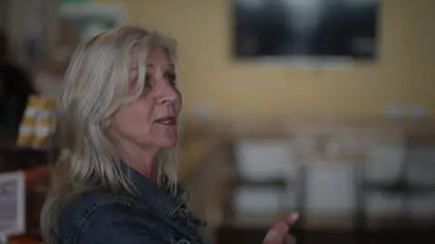 Michelle Delaney has long blonde hair and is side on to camera