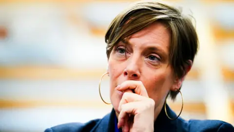 PA Media A picture of Jess Phillips looking to the left side of where the photo was taken. She looks pensive and has her hand in front her mouth. She has short cropped hair and is wearing large hoop earrings.