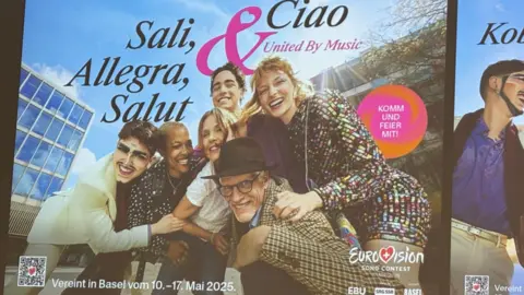 EBU A poster of a diverse crowd of people laughing and huddling in for a photo. The poster says: Sali, Allegra, Salut & Ciao, United by music, as well as the Eurovision logo. 
