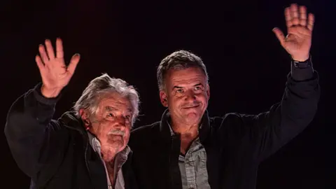 Getty Images Former President of Uruguay José Mujica and presidential candidate for the Frente Amplio party Yamandu Orsi greet their supporters at the closing campaign rally in April 2024 in Montevideo, Uruguay. (Photo by Ernesto Ryan/Getty Images)