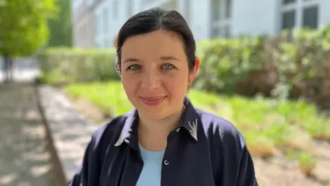Natalia Panchenko, with dark hair and in a dark shirt looks directly at the camera