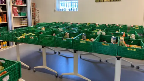 A room has tables laden with green crates with fresh vegetables and milk inside them.