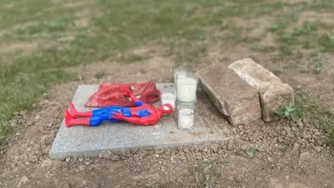 A paving stone with a Spider Man action figure on it and a couple of white candles.