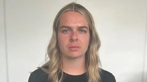 Katherine Errington looks directly at the camera. She has long blonde hair and is wearing a black top