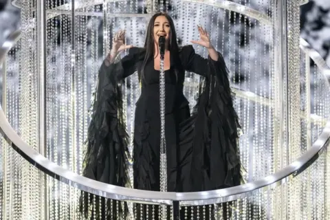 EPA-EFE/Shutterstock Israel's entry Yuval Raphael performs during rehearsals in a black dress surrounded by a detailed sparkled stage prop.