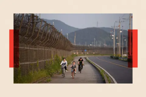 AFP via Getty Images People on bicycles along a barbed wire fence of the Demilitarized Zone