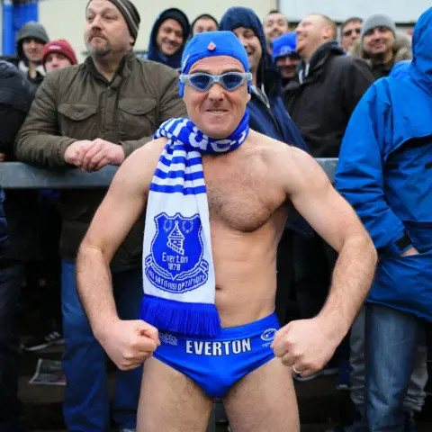 Getty Images Speedo Mick doing a bodybuilder pose in his trunks, an Everton scarf, swimming cap and goggles, on the terraces surrounded by fully clothed fellow fans at Everton's FA Cup game at Carlisle United in 2016.