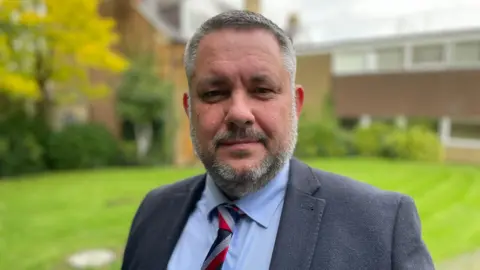 Sam Read/BBC Former Conservative council leader Jason Smithers standing outside in a suit and chequered tie.