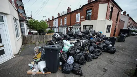Getty Images A huge pile of bin bags on a residential street. There are dozens of refuse sacks with terraced homes in the background.