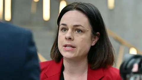 Getty Images Kate forbes mid speech. She has a brown shoulder length bob and is wearing a red blazer