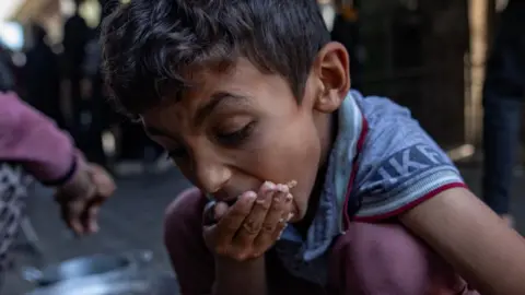 EPA A Palestinian boy crouching down and eating with his right hand