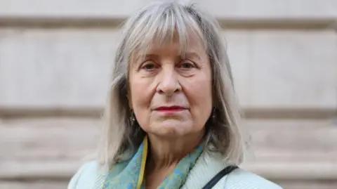 Getty Images A woman with shoulder length greying hair and a pale green jacket stares directly at the camera
