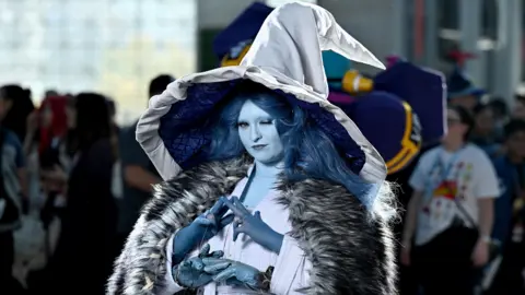 Getty Images A fan of Elden Ring at last year's Comnic Con in New York dressed as Elden Ring's Ranni the Witch, in a grey gown, huge silver hat, fur cape and blue skin make-up, with an extra set of arms and hands and long, blue hair