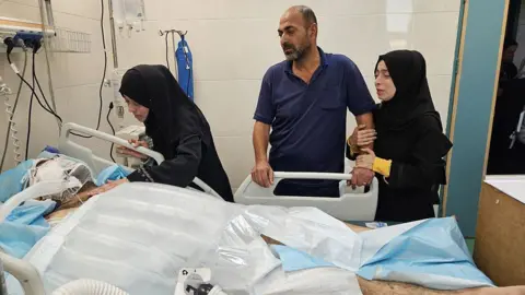 Getty Images Alaa al-Najjar (2nd L) visits her husband (L) in Nasser hospital