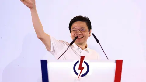 Reuters Singapore PM Lawrence Wong smiles with both his arms held aloft as he addresses a crowd at an election rally