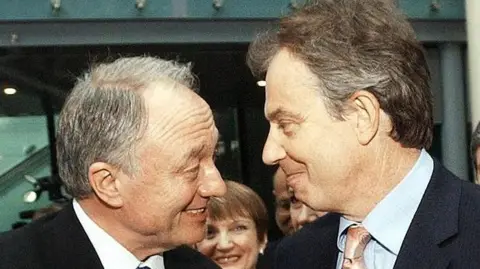 Getty Images A close up of Tony Blair and Ken Livingstone, both smiling, facing each other. Tessa Jowell is visible in the background.