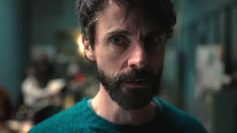 Netflix Close up of a man wearing a green jumper staring off to the right of the camera.
