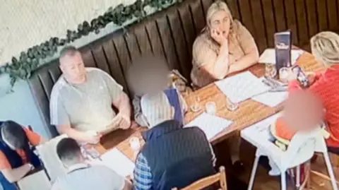 Bella Ciao The family at Bella Ciao sitting around a wooden table. Bernard and Ann are sitting on a long bench with a leather brown back, while others sit opposite them, including a child in a white high chair.