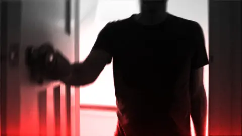 Getty Images A dark silhouette of a person wearing a short-sleeved shirt is positioned in the foreground, facing a door. The person is using their left hand to grasp and turn a doorknob. The background is brightly illuminated, casting the figure into deep shadow and creating a high-contrast effect. A red gradient overlays the bottom portion of the image, contributing to an eerie or dramatic atmosphere