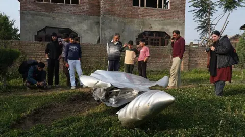 NurPhoto via Getty Images People look at a part of an aircraft in Wuyan village in the Himalaya region of Kashmir on May 7, 2025. India fires missiles at Pakistani territory early on May 7, killing at least eight people, according to Pakistan, which says it has begun retaliating in a major escalation between the nuclear-armed rivals. (Photo by Sajad Hameed/NurPhoto via Getty Images)