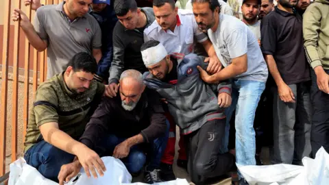 Reuters Palestinian men mourn beside the bodies of relatives killed in Israeli air strikes, at Nasser hospital, in Khan Younis, southern Gaza (15 May 2025)
