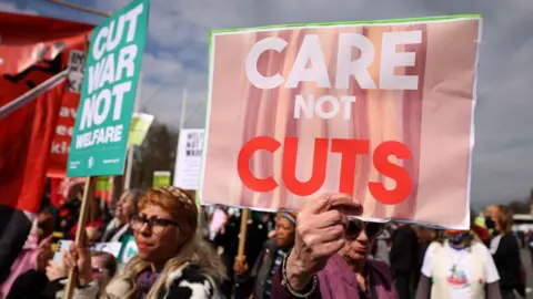 EPA Protesters demonstrate against disability and welfare cuts during the announcement of the Spring Statement outside Parliament in London in March. They hold up placards reading: "Care not cuts".