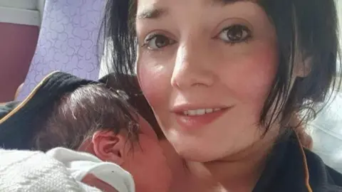 Niki Cotson Niki Cotson cradling her newborn son while lying on a hospital bed. Both have dark hair, with Niki's being in a short bob cut.