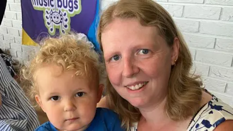 BBC A woman with ginger hair in a blue and white patterned top with a small child with ginger curly hair