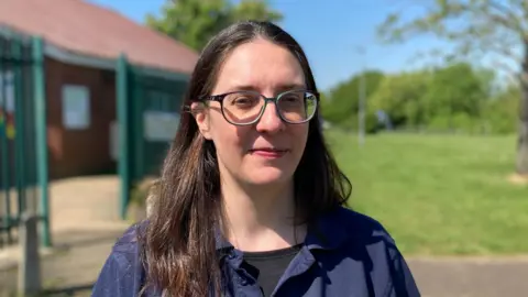 BBC Headshot of Charis standing outside with the community centre in the background and a grassy field.