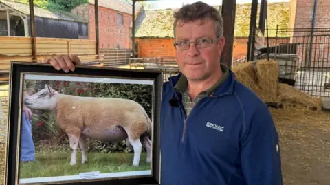 BBC Farmer David Thornley holds a framed picture of one of his prize-winning rams