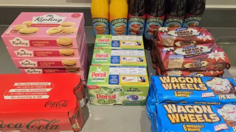 Peter in Lancashire A multipack of Coca-Cola, six packs of Mr Kipling Viennese Whirls, six bottles of Robinsons squash, four packs of McVities Jamaica Ginger cakes, several packs of Wagon Wheel and three boxes of Persil washing tabs are arranged in a display of Peter's discounted Co-op Deliveroo order.