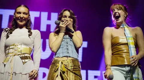 Getty Images Remember Monday smile and laugh on stage as they get a warmer-than-anticipated welcome from Eurovision fans. Holly-Anne, in the centre, clasps her hands over her mouth in surprise.