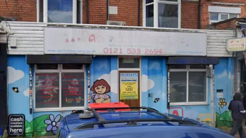 Google The outside of Daffodils Nursery in Smethwick. The walls are painted in a mural showing blue sky and flowers and a character standing by the door. There is a faded sign above the entrance in Waterloo Road.