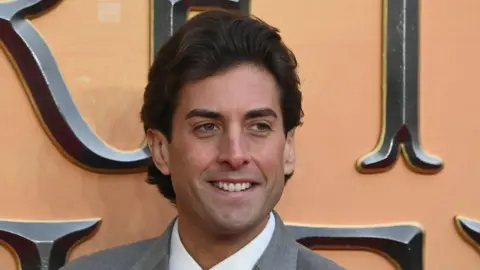 Getty Images James Argent smiling at a red carpet event. He has dark hair swept backwards and is wearing a grey suit jacket and white shirt.